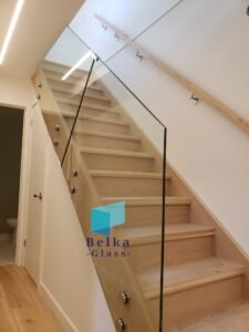 Modern frameless glass railing on wooden staircase installed by Belka Glass in Toronto, fully compliant with Ontario Building Code safety standards