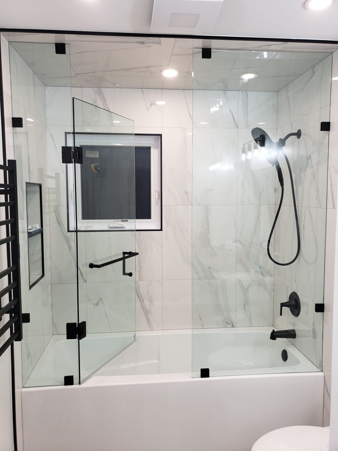 Frameless glass shower enclosure installed over bathtub in Toronto by Belka Glass, featuring black hardware and modern design