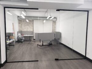 Frameless glass office partition with black metal framing and sliding door, installed in a modern Toronto office by Belka Glass.