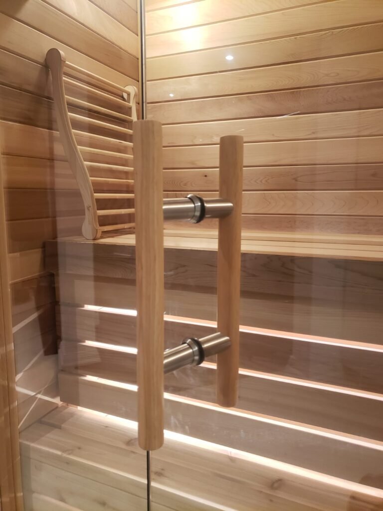 Wooden handle detail on frameless glass sauna door, part of a custom home sauna installation in Toronto by Belka Glass.